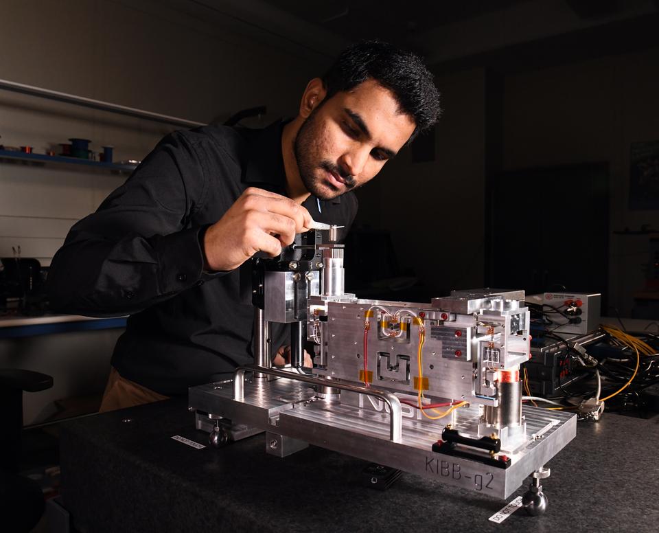 A person in a black shirt works on a mechanical device in a lab setting.